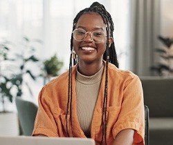 Woman with glasses smiling while working on laptop