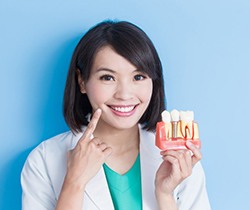 Coppell implant dentist points to her smile while holding model of dental implants