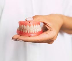 person in white lab coat holding full dentures