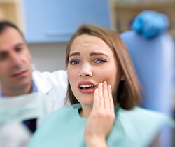 Woman in dental chair holding cheek