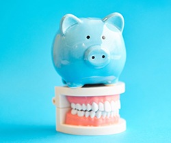 Piggybank on top of false teeth on blue background