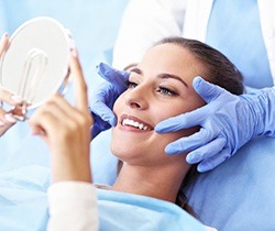 woman sitting in dental chair and smiling at hand mirror