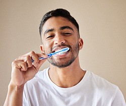 Man in white shirt smiling while brushing his teeth