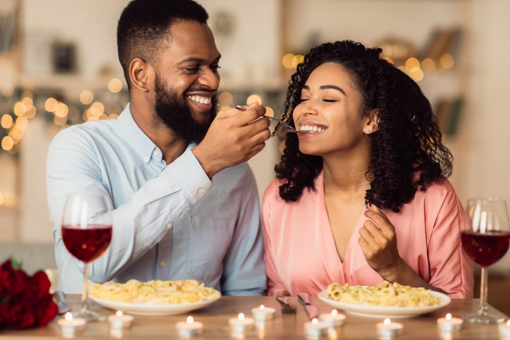 Man smiling while giving his partner a bite of his pasta