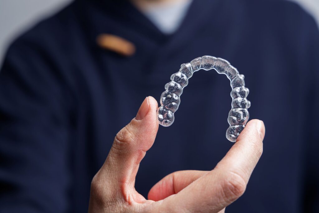 Man in navy scrubs holding clear aligner